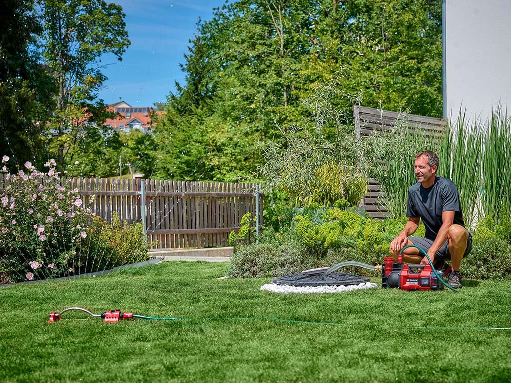 A man watering flowers in his garden with rainwater and the help of a garden pump.