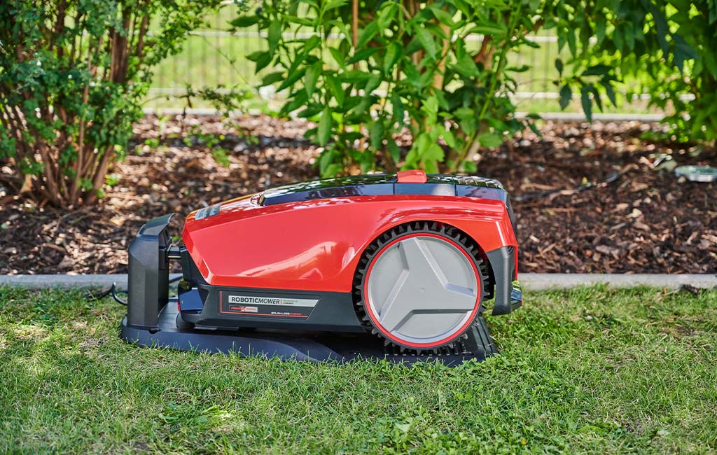 A red and black robotic lawnmower in a charging station in the garden.