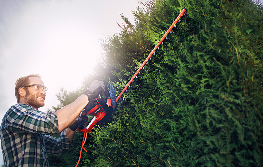 a man is trimming a hedge with a Einhell hedge trimmer