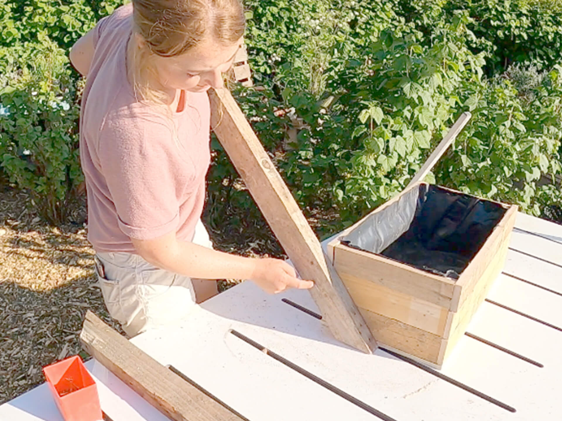 Woman attaching a wood piece onto the side of the herb planter. 