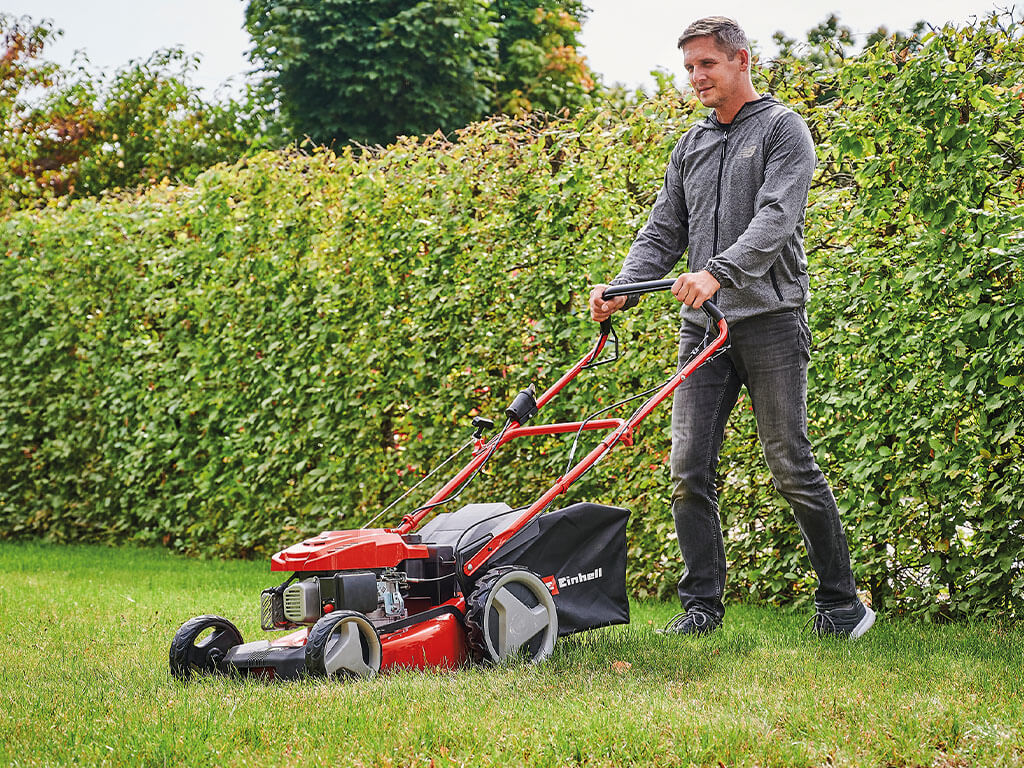 A man mows the lawn in his garden with a powerful petrol lawnmower from Einhell.