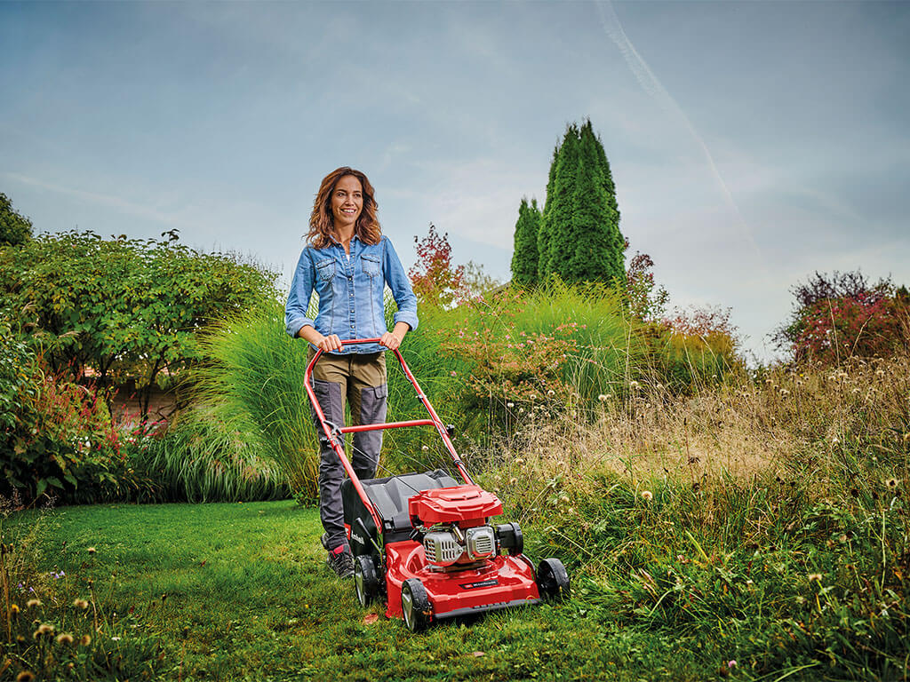 A woman cuts tall grass with a powerful petrol lawnmower from Einhell.