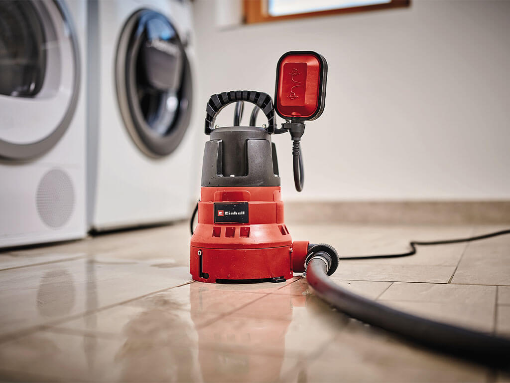 A flat-suction water pump from Einhell stands on wet tiles.