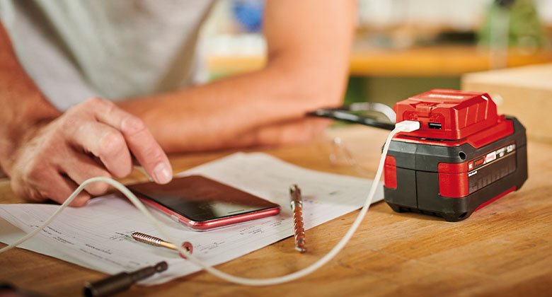 Man using a Power X-Change battery with USB adapter as a powerbank to charge his smartphone