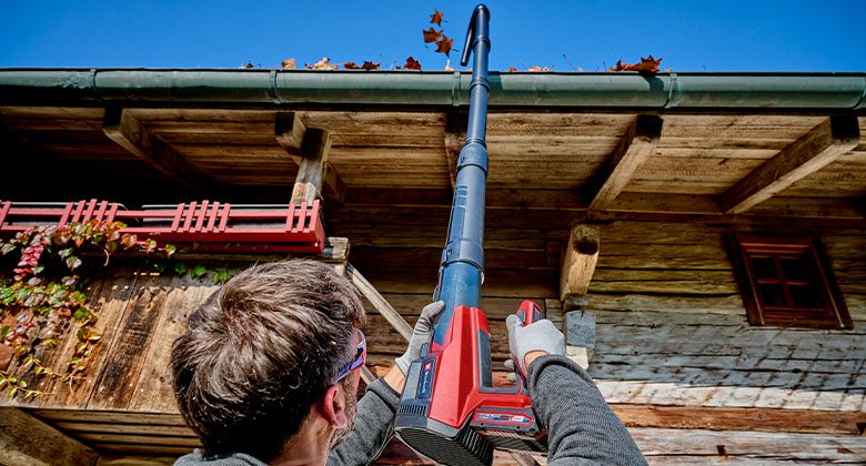 Man blowing leaves from gutter with a leaf blower and extension