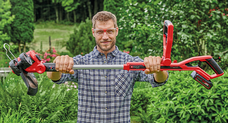 a man holds an Einhell trimmer in a garden